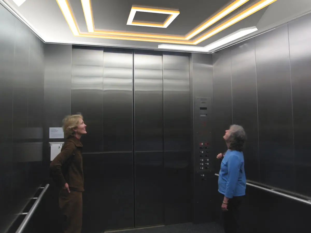 Elevator Cab Lighting Ideas illustrated with two women standing in a well lit elevator - Elevator Cab Lighting Ideas: Enhancing Ambiance and Functionality - Vorlane - Vorlane Elevator Cab Lighting Ideas illustrated with two women standing in a well lit elevator - Elevator Cab Lighting Ideas: Enhancing Ambiance and Functionality - Vorlane - Vorlane